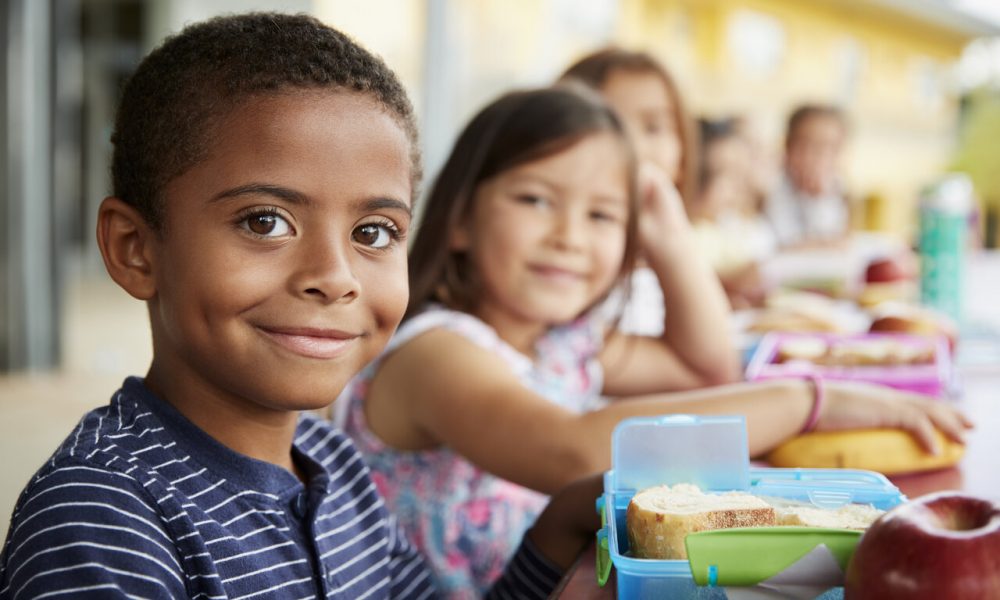 Young boy and girl at school lunch table smiling to camera