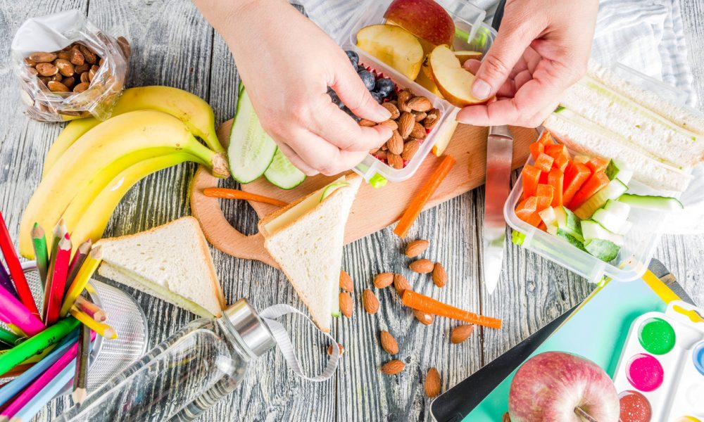Mother cooking school lunch box set, Preparing healthy snacks - cheese sandwich with cucumber, carrot. nuts, fruits and vegetable in box.